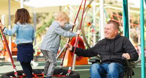 A dad in a wheelchair playing with his kids on the playground.