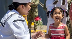 A young girl hands her mom in uniform a flower